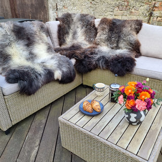 En udendørs sofa med 3 engelske lammeskind om sommeren, med et lille bord der er dækket op til en hygge stund.