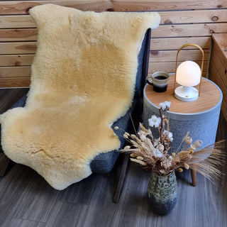 Lyst, korthåret lammeskind til baby på en lænestol ved et lille sidebord.