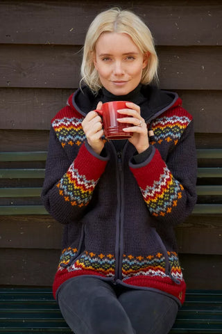 Pachamama-cardigan med farverige strikkede mønstre, båret af en model med en kop.