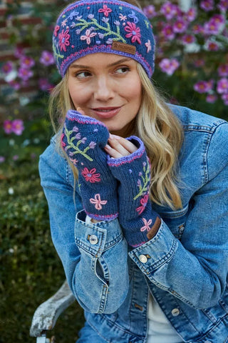 Blå pulsvarmere i uld med broderede blomster og lilla kanter, vist på hænderne.