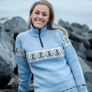 Lyseblå norsk uldtrøje med lyst mønsterbånd og kort lynlås, båret af en model.