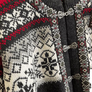 Den koksgrå norske uldcardigans hvide mønster, røde detaljer og tinhægter, vist tæt på.