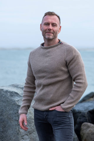 Beige Jurmo-uldtrøje fra WOOLWEAR med rund hals, båret af en model ved kysten.