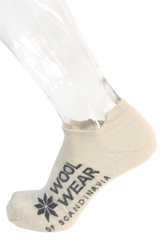 Lys merinouldfootie med WOOL WEAR-logo, vist på en fod.