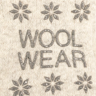 Hvide uldsokkers sål med blomsterformede skriddupper og WOOL WEAR-logo, vist tæt på.