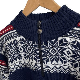 Blå ribkrave, lynlås og lyst nordisk mønster på den marineblå merinouldsweater, vist tæt på.