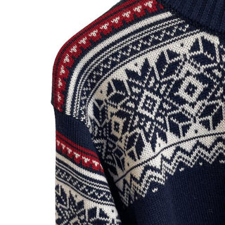 Skulder på den marineblå merinouldsweater med hvidt nordisk mønster og rødt bånd.