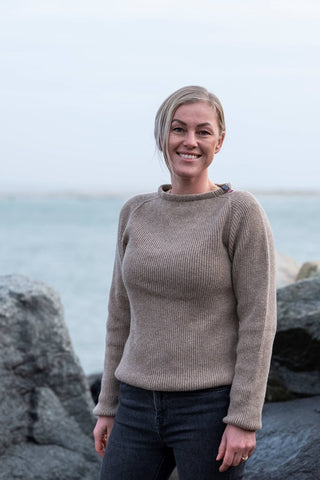 Beige Jurmo-uldtrøje fra WOOLWEAR med rund hals, vist på en model foran havet.